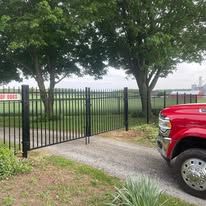 A red truck is parked in front of a metal fence.