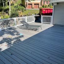 A gray deck with a white railing and chairs on it.
