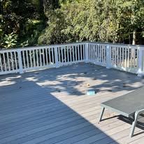 A wooden deck with a white railing and chairs on it.