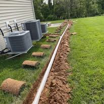 A drain pipe is being installed in a yard next to a house.