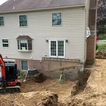 An excavator is digging a hole in front of a house.