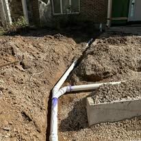 A pipe is being installed in the dirt in front of a house.
