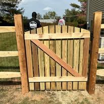 A man is standing behind a wooden fence with a wooden gate.