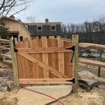 A wooden gate is sitting next to a fence in front of a house.