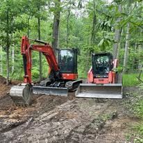 A red excavator and a small bulldozer are sitting on top of a dirt road in the woods.