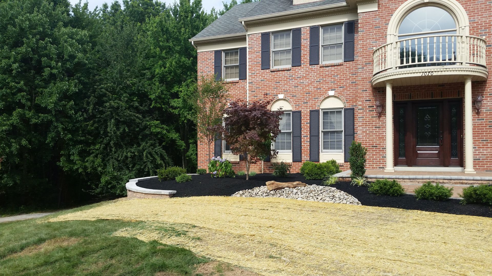 A brick two-story house with a newly landscaped front yard featuring fresh black mulch and straw-covered grass.