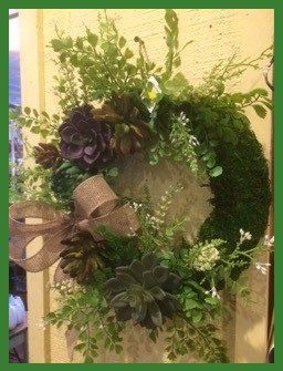 A wreath with flowers and moss is hanging on a door.