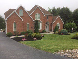 A large brick house with a lush green lawn and a driveway in front of it.