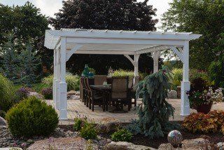 A white pergola with a table and chairs underneath it in a garden.