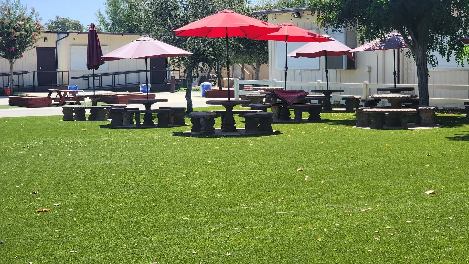 Picnic tables with red umbrellas on green turf, outdoor setting.