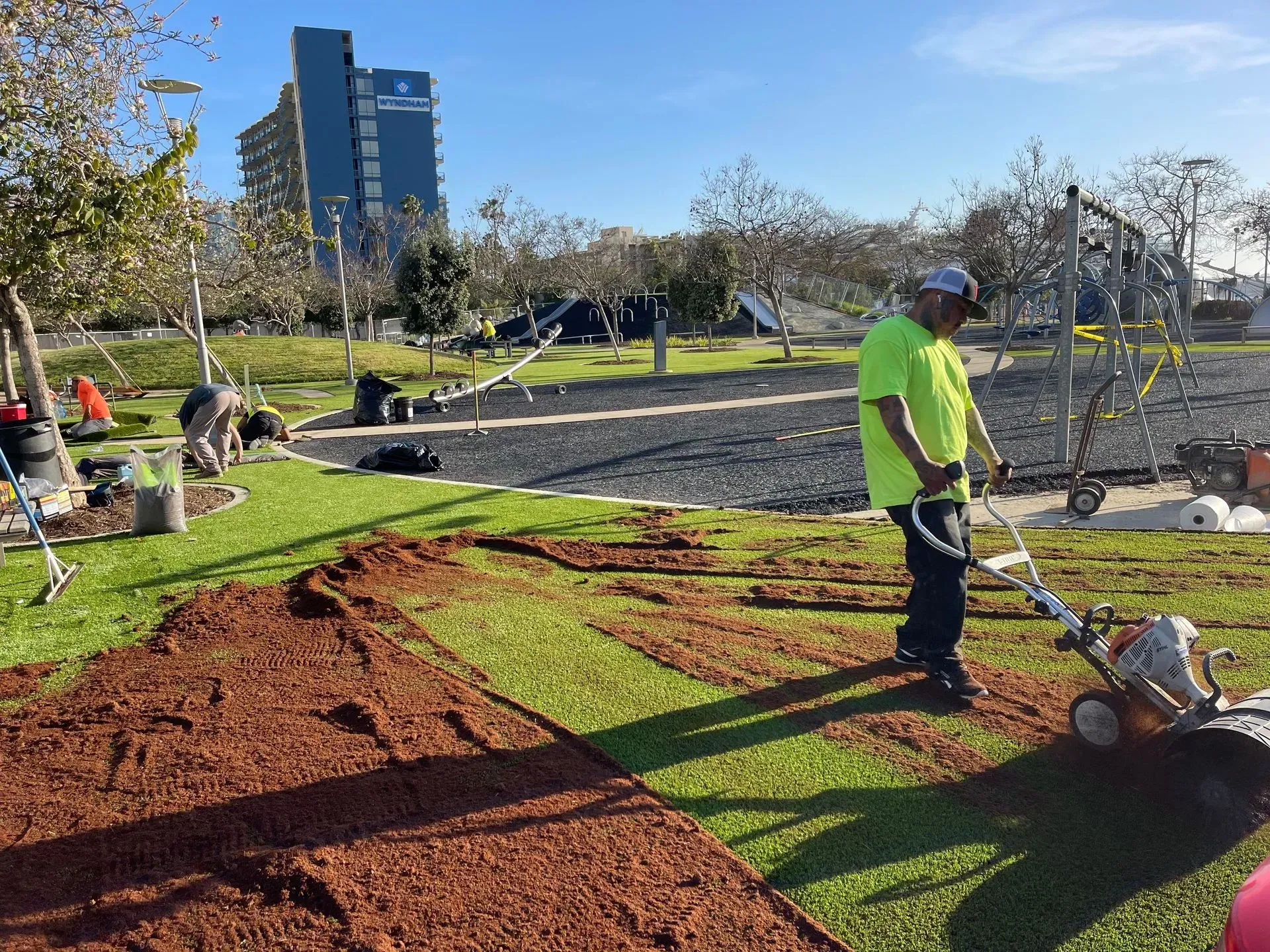 A groundskeeper using a machine to aerate artificial turf in a park setting.