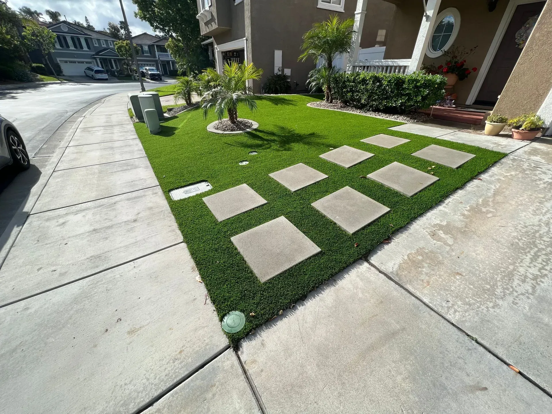 Artificial green lawn with square stepping stones in front of a house.
