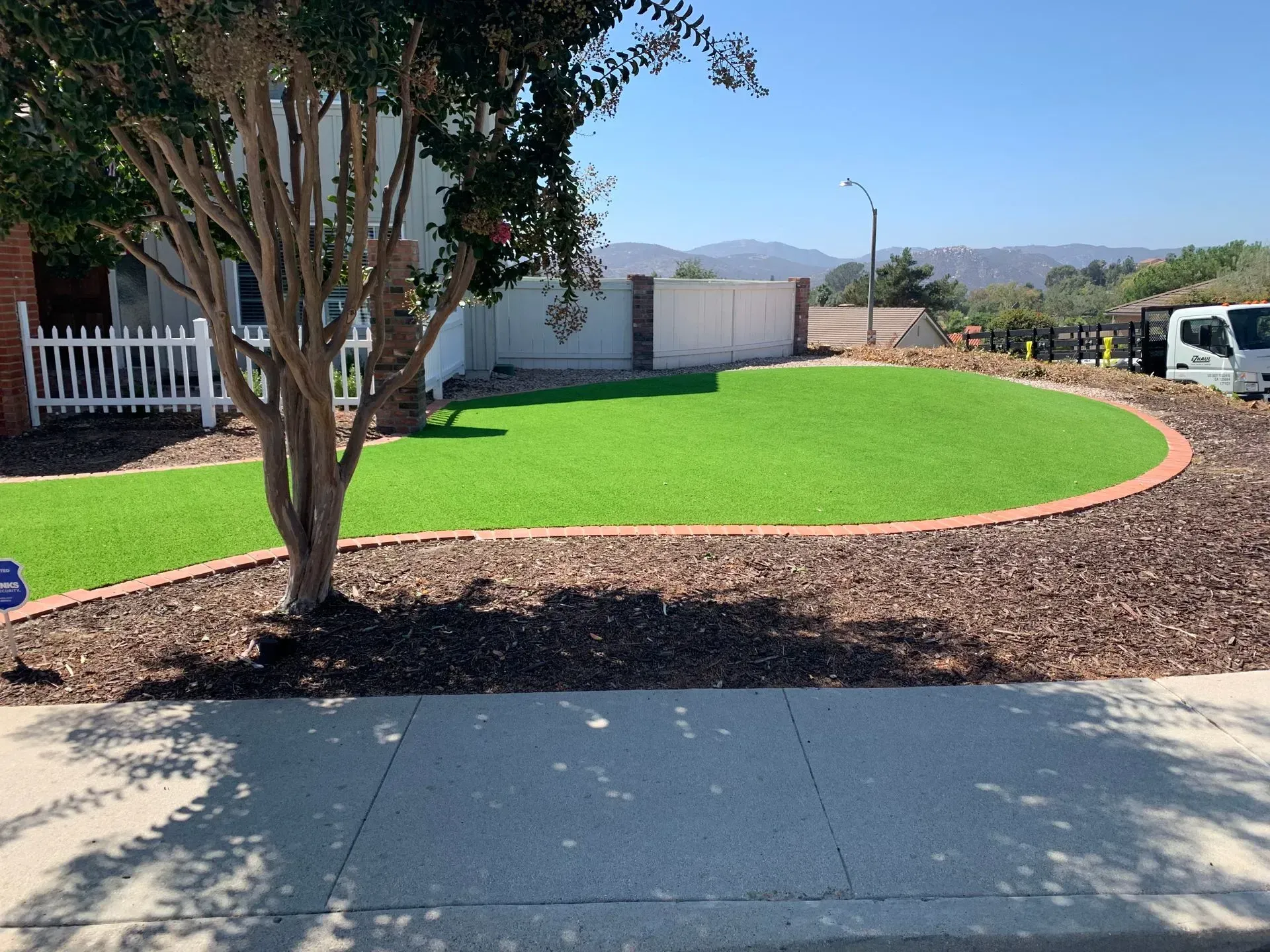 Front yard with a green lawn, edged with red brick and brown mulch, tree in foreground.