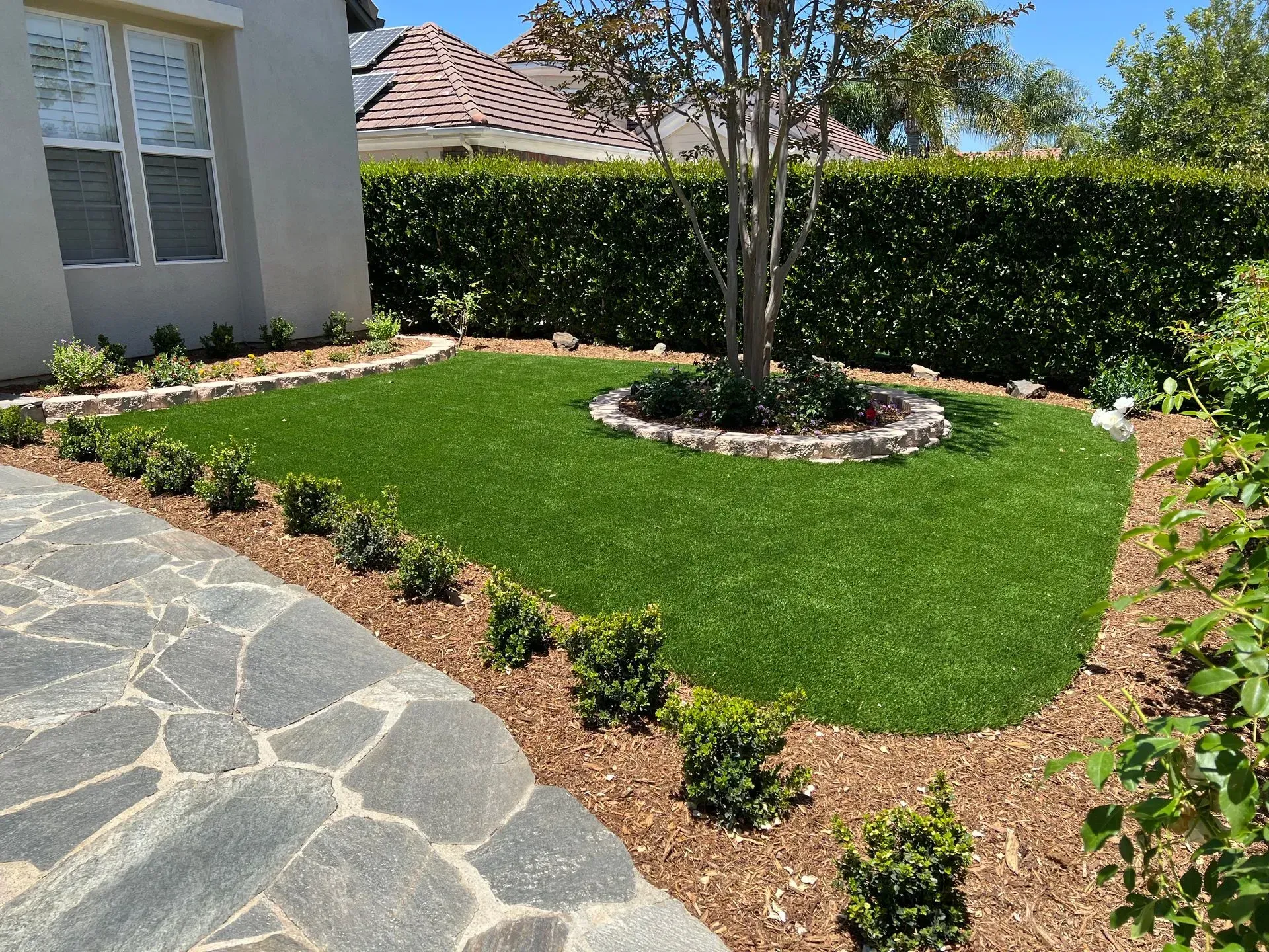 Manicured front yard with green lawn, shrubs, stone walkway, and tree.