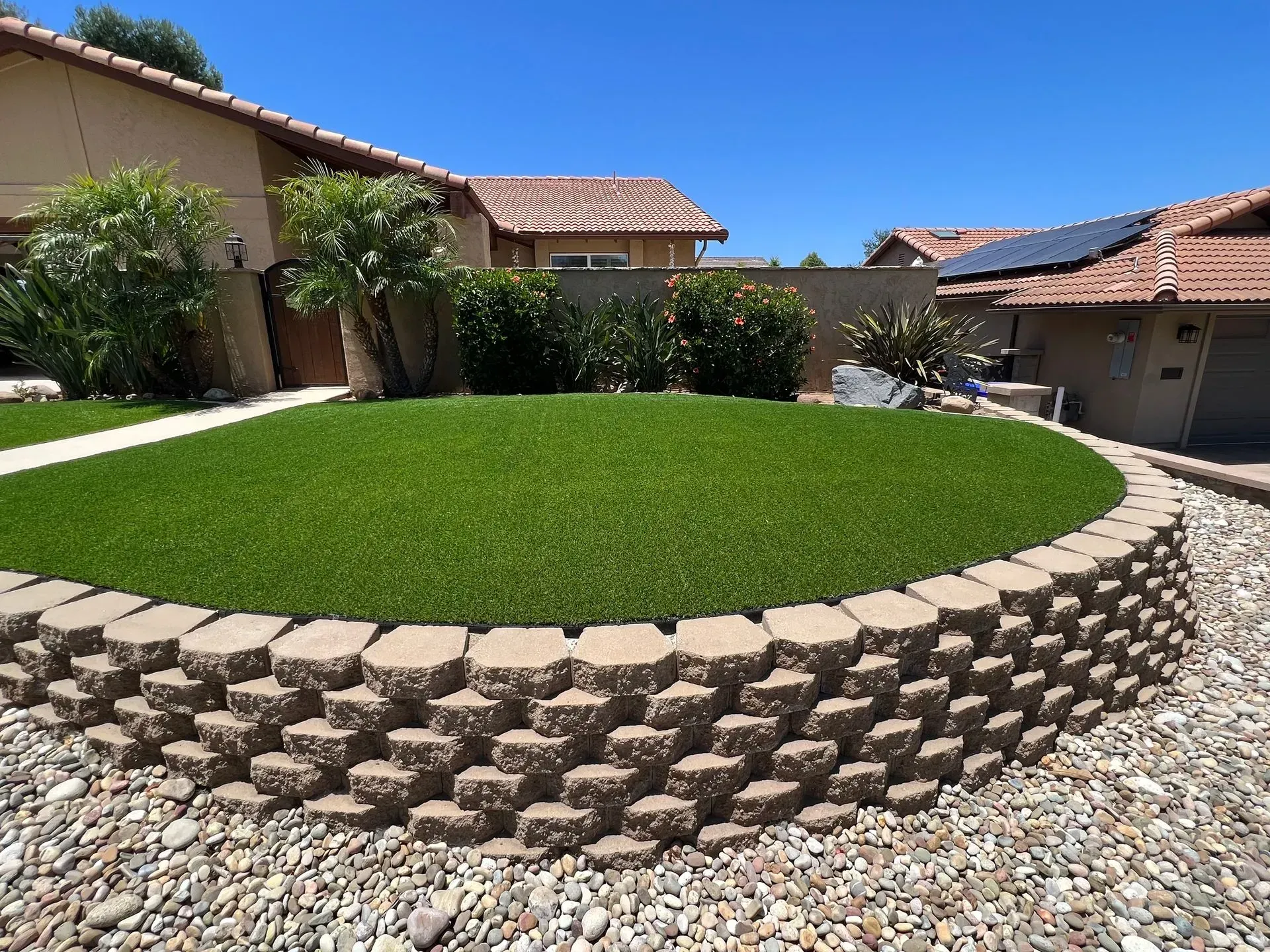 Green lawn on a raised bed with a brick retaining wall; house and blue sky in background.