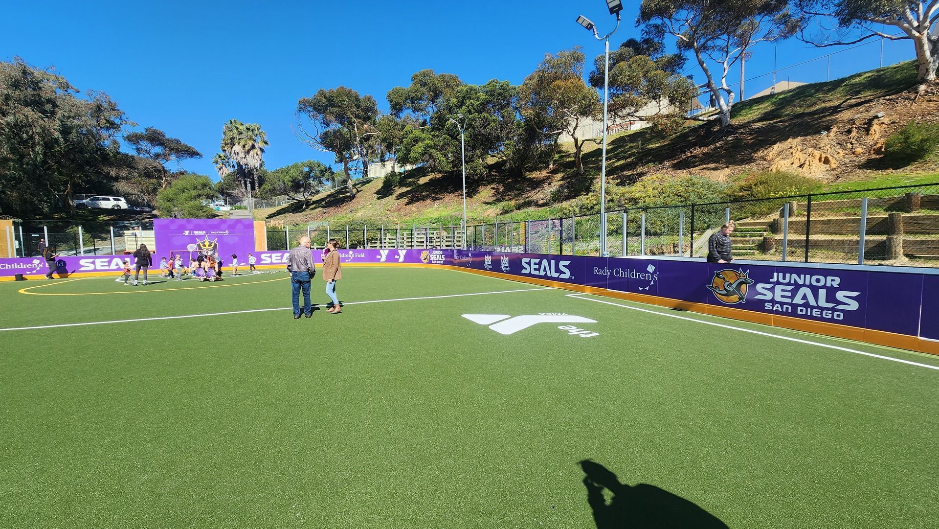 People on a green field with purple and gold borders, sunny day.