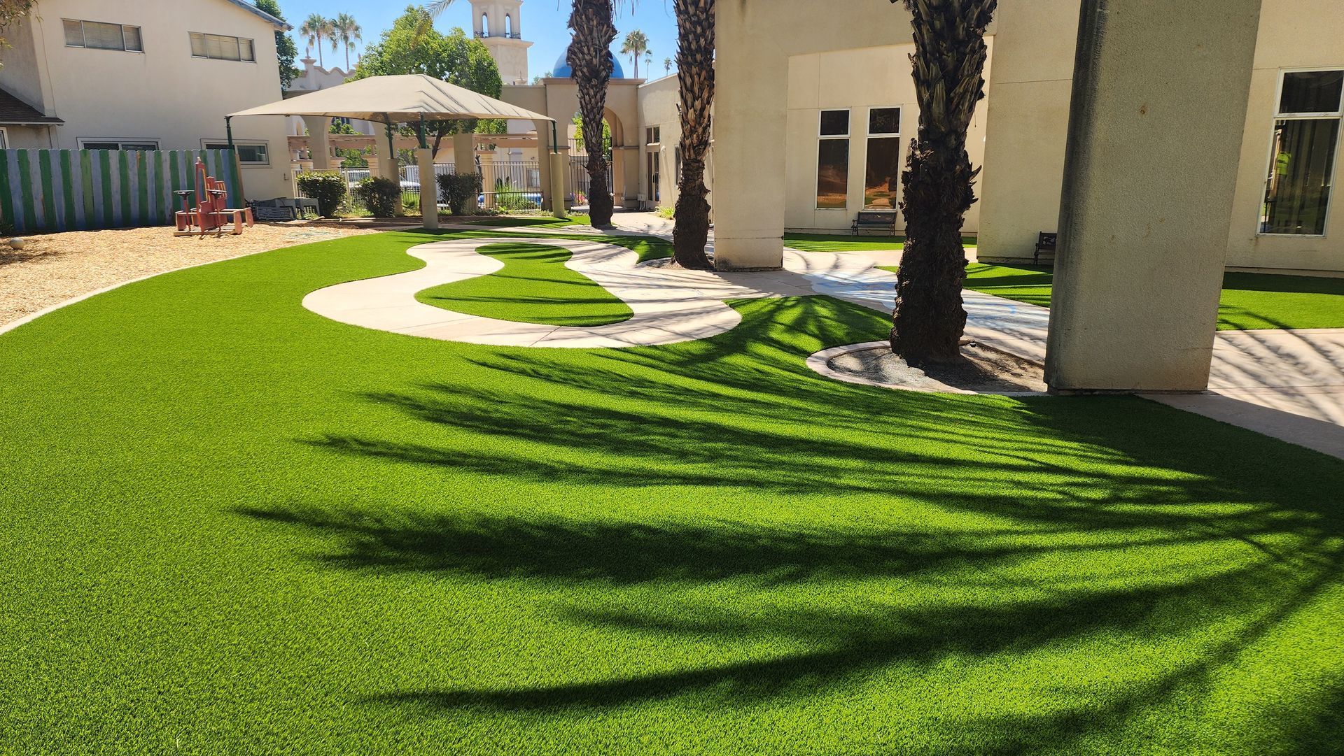 Green lawn with palm tree shadows, white walkway, gazebo in outdoor setting.
