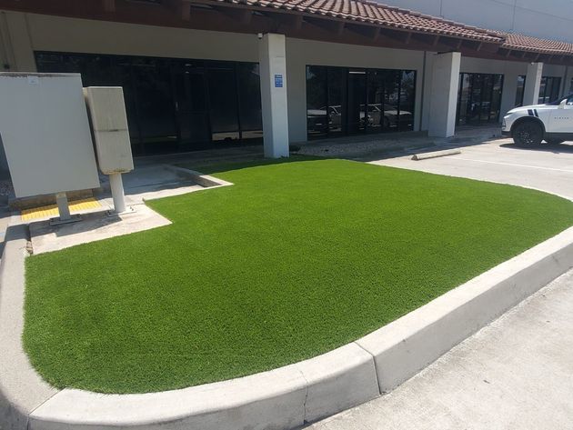 Artificial green turf near a building with a white truck parked nearby. 