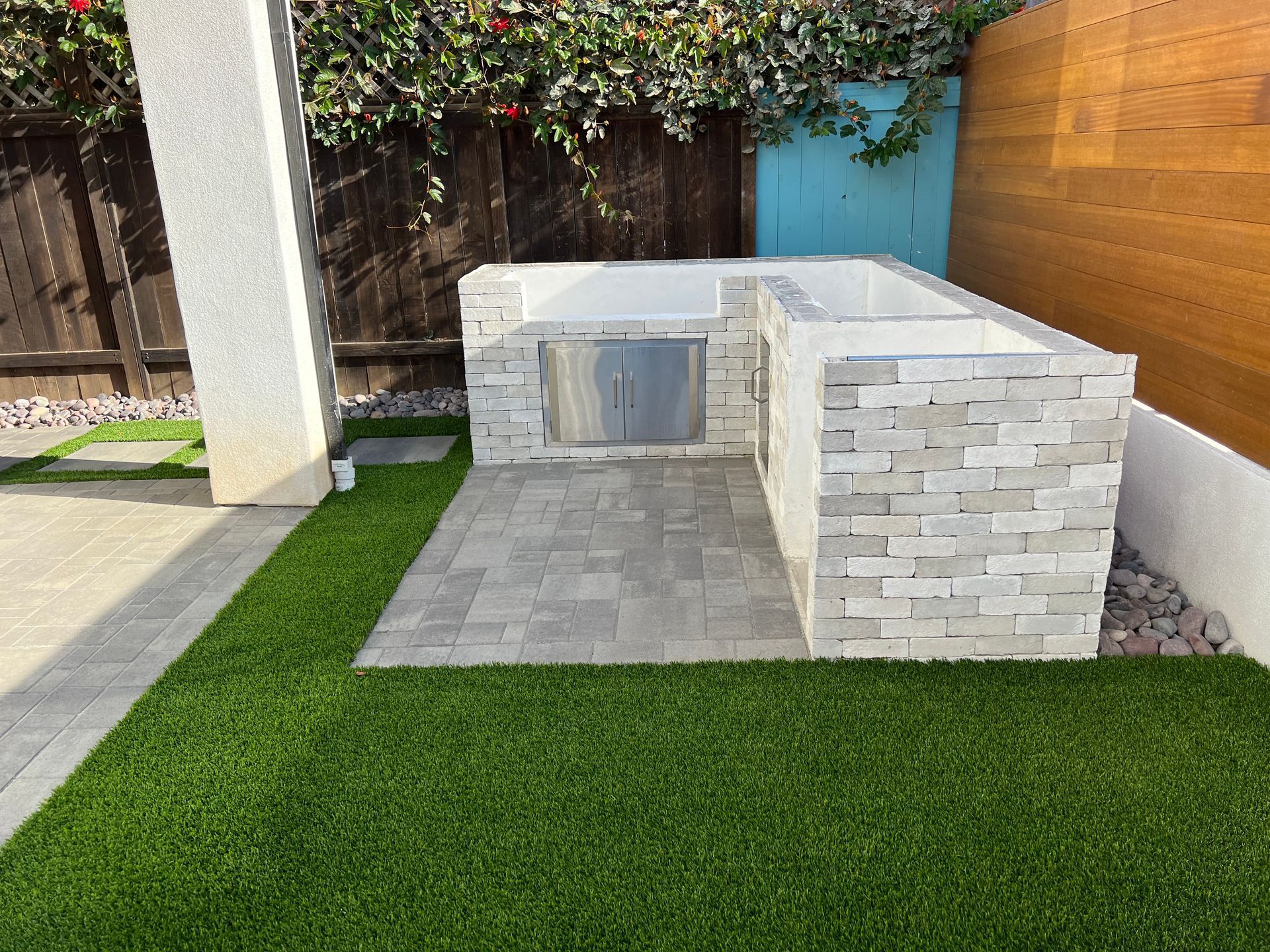 Outdoor kitchen with stone facade, gray patio, and green turf.