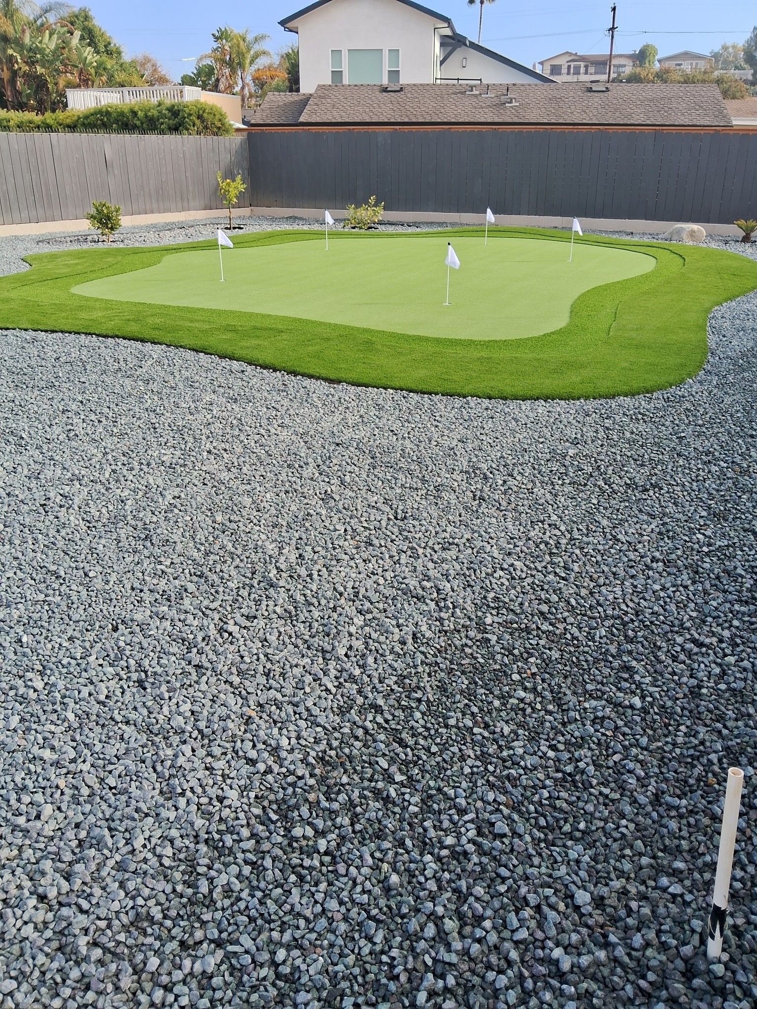 A backyard putting green with white flagsticks surrounded by gravel.