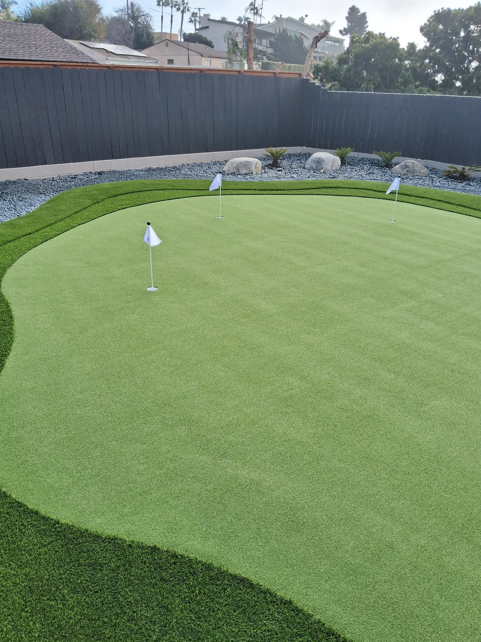 Artificial turf putting green in backyard with white flags.