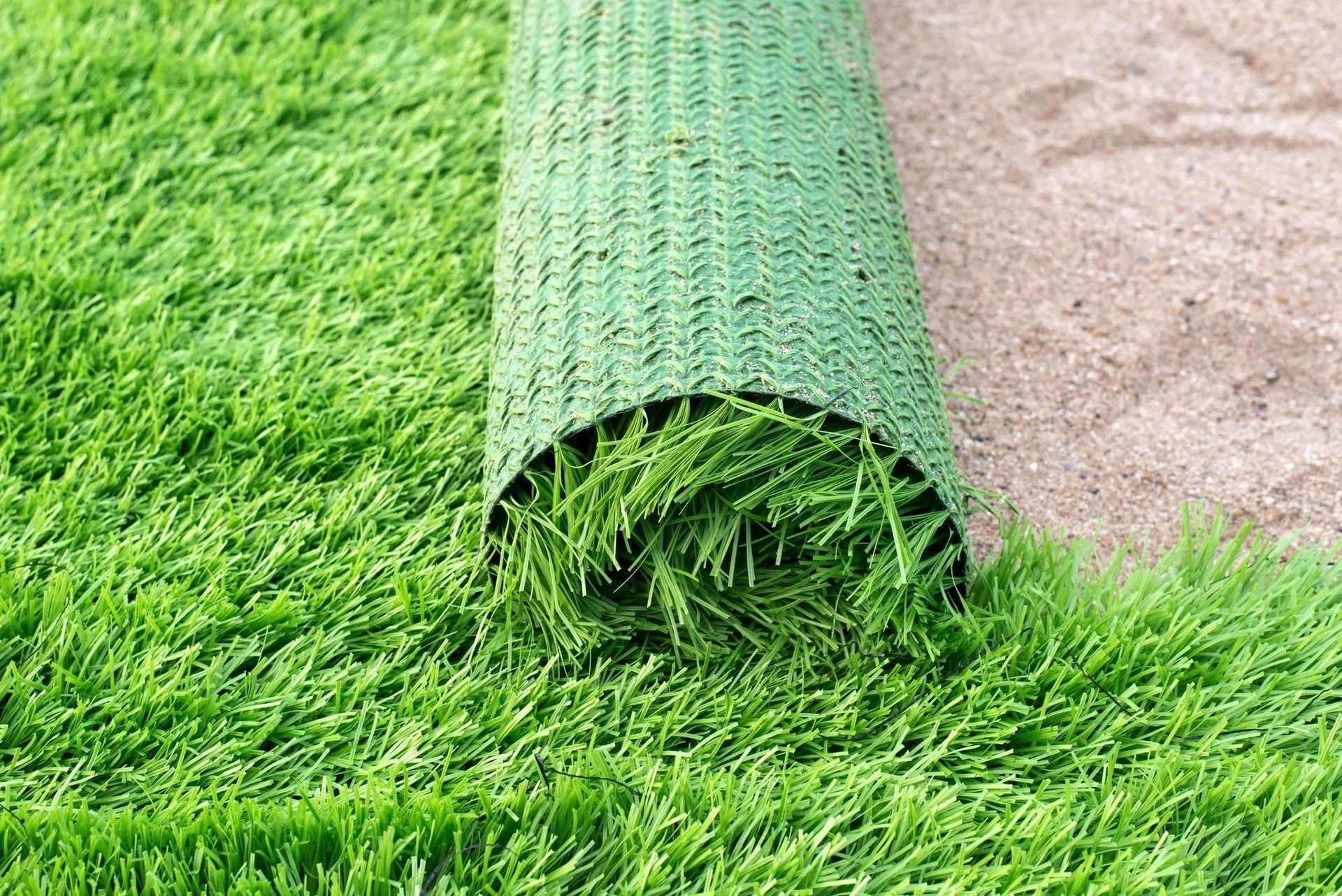 Green artificial turf rolled out on sandy ground.