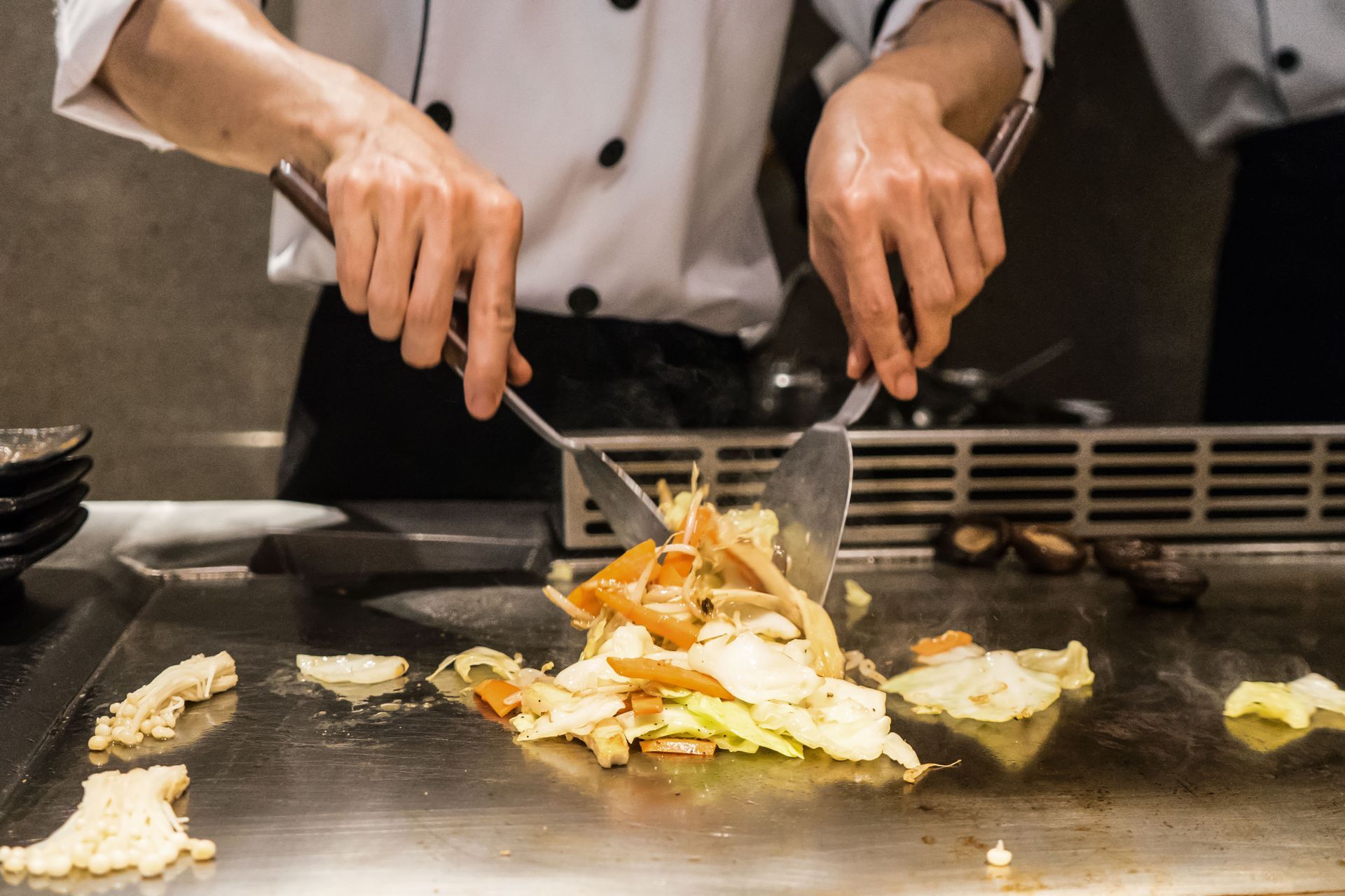 Chef cooking vegetables on a flat top grill in a restaurant kitchen.