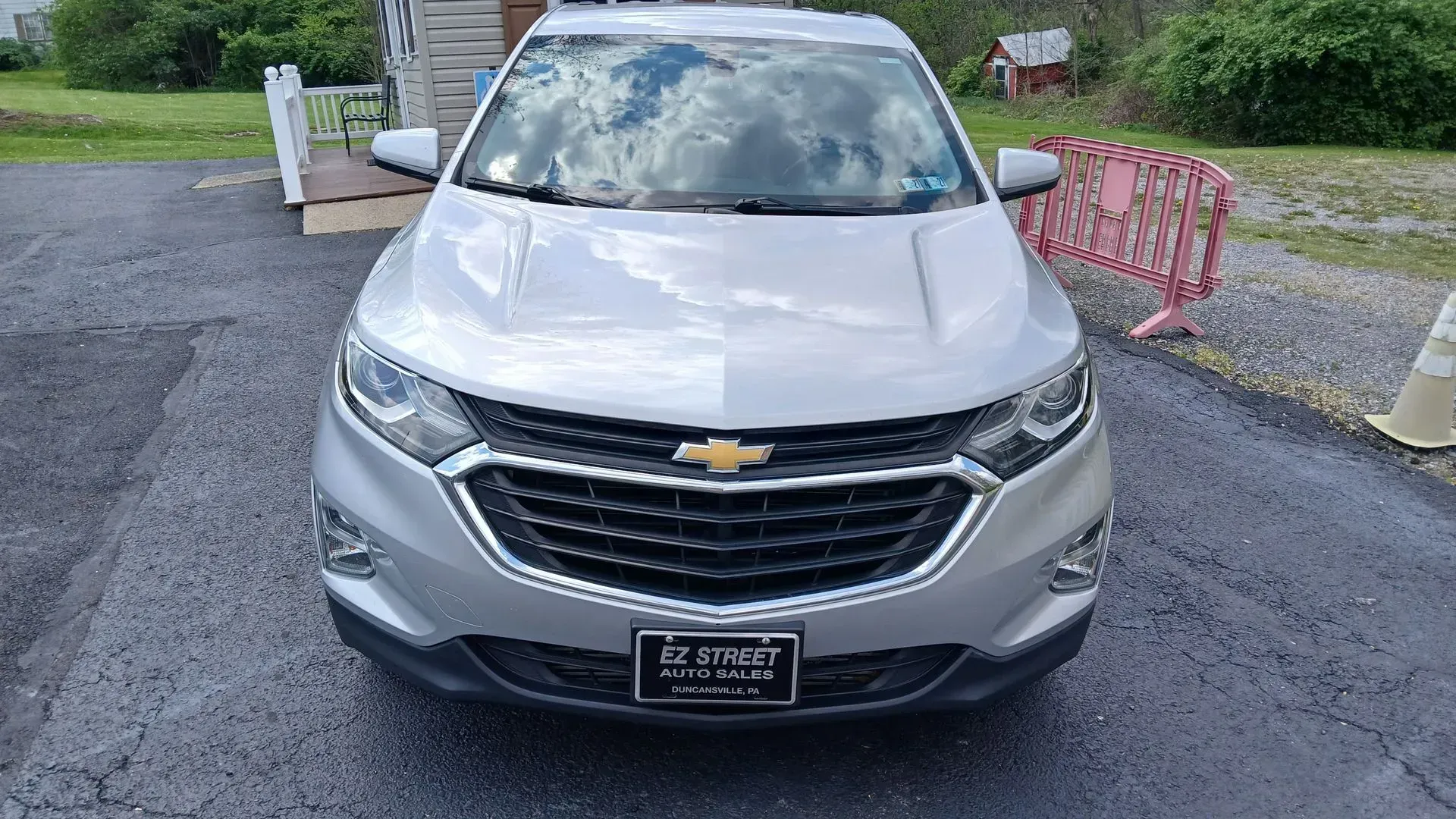 Front view of a silver Chevrolet SUV parked on a gravel driveway near a red gate.