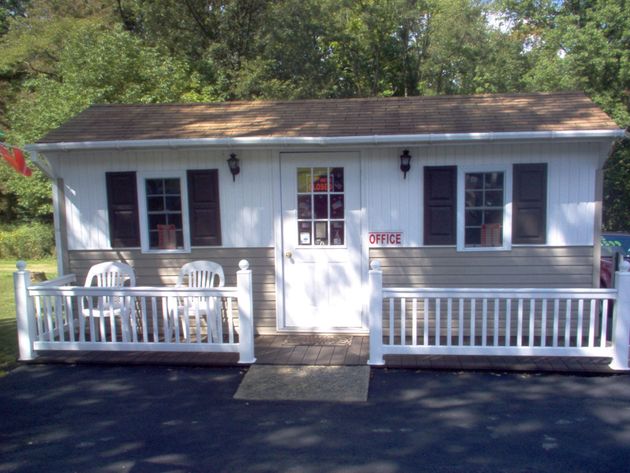 A small, white and tan office building with two windows, brown shutters, a central door, and a white picket fence porch.