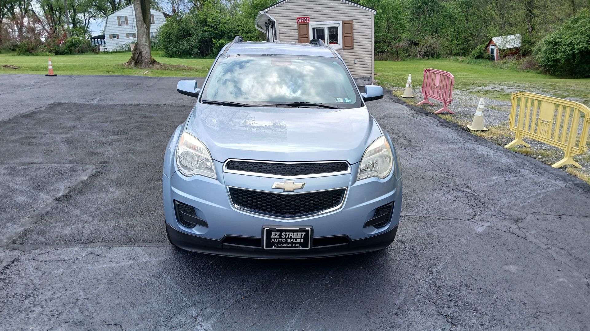 Light blue car parked on a gravel driveway in front of a small building and trees.
