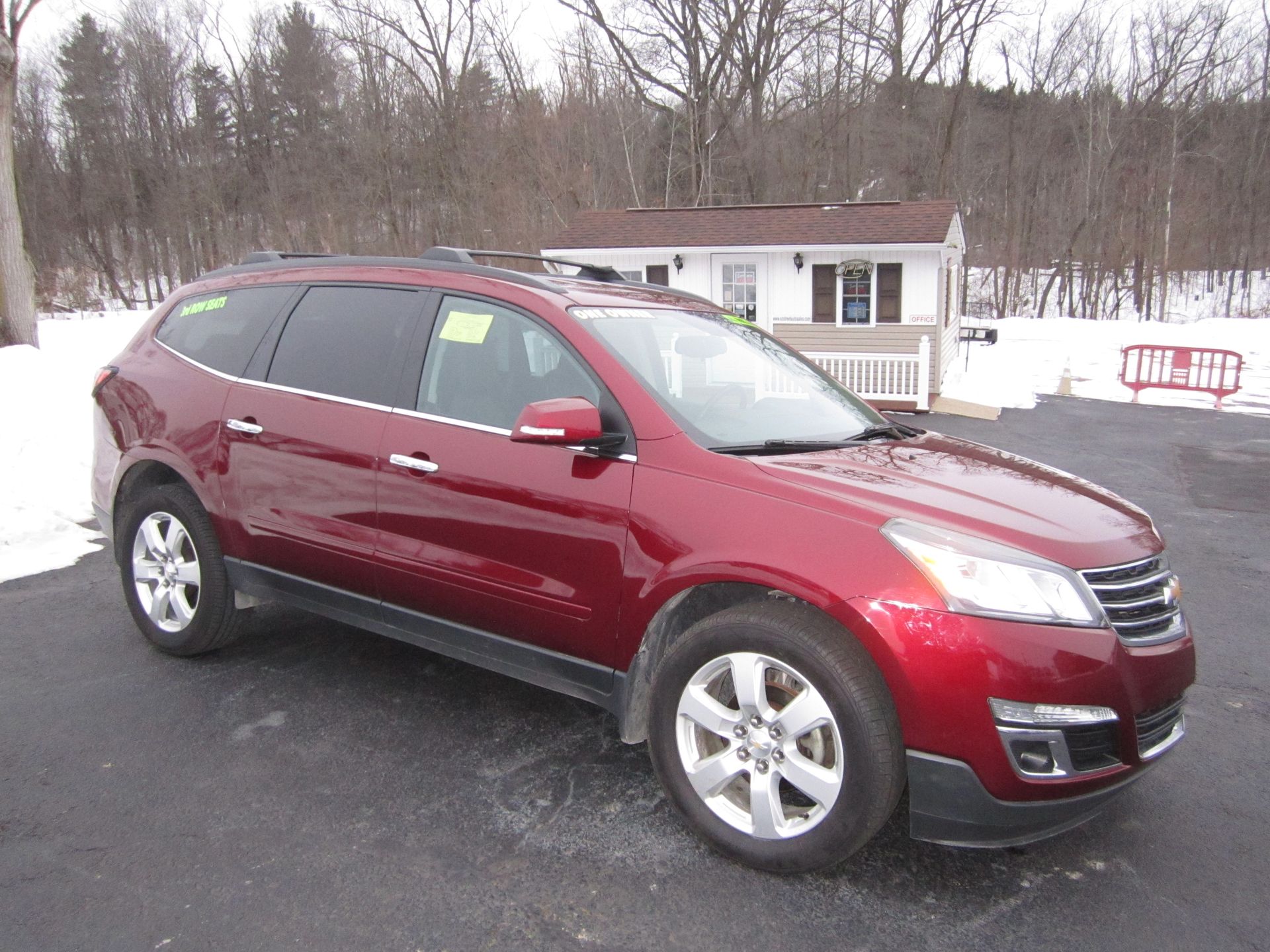 A deep red, mid-size SUV parked on an asphalt lot with snow in the background.
