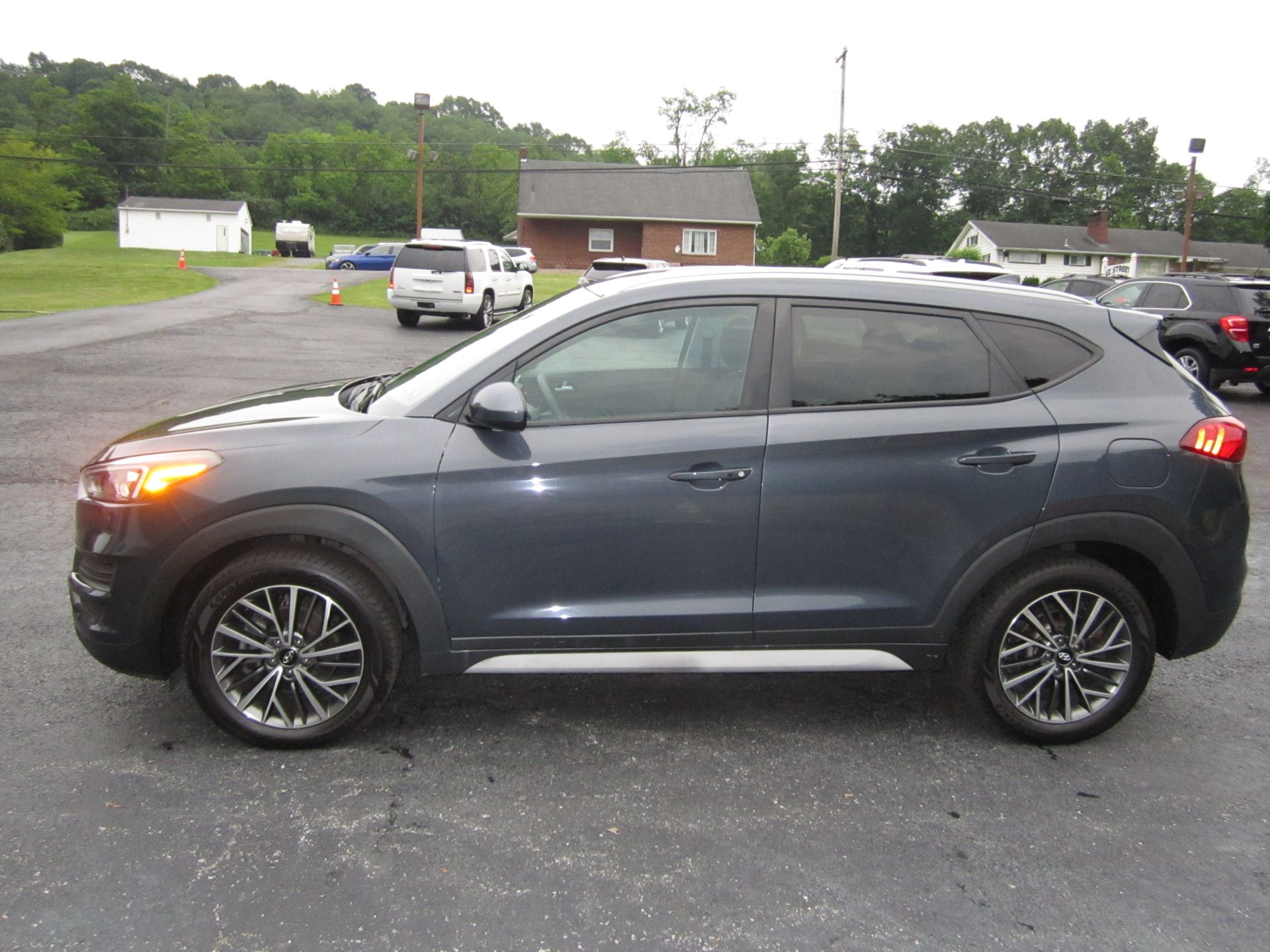 A dark grey SUV parked on an asphalt lot with a brick building and trees in the background.