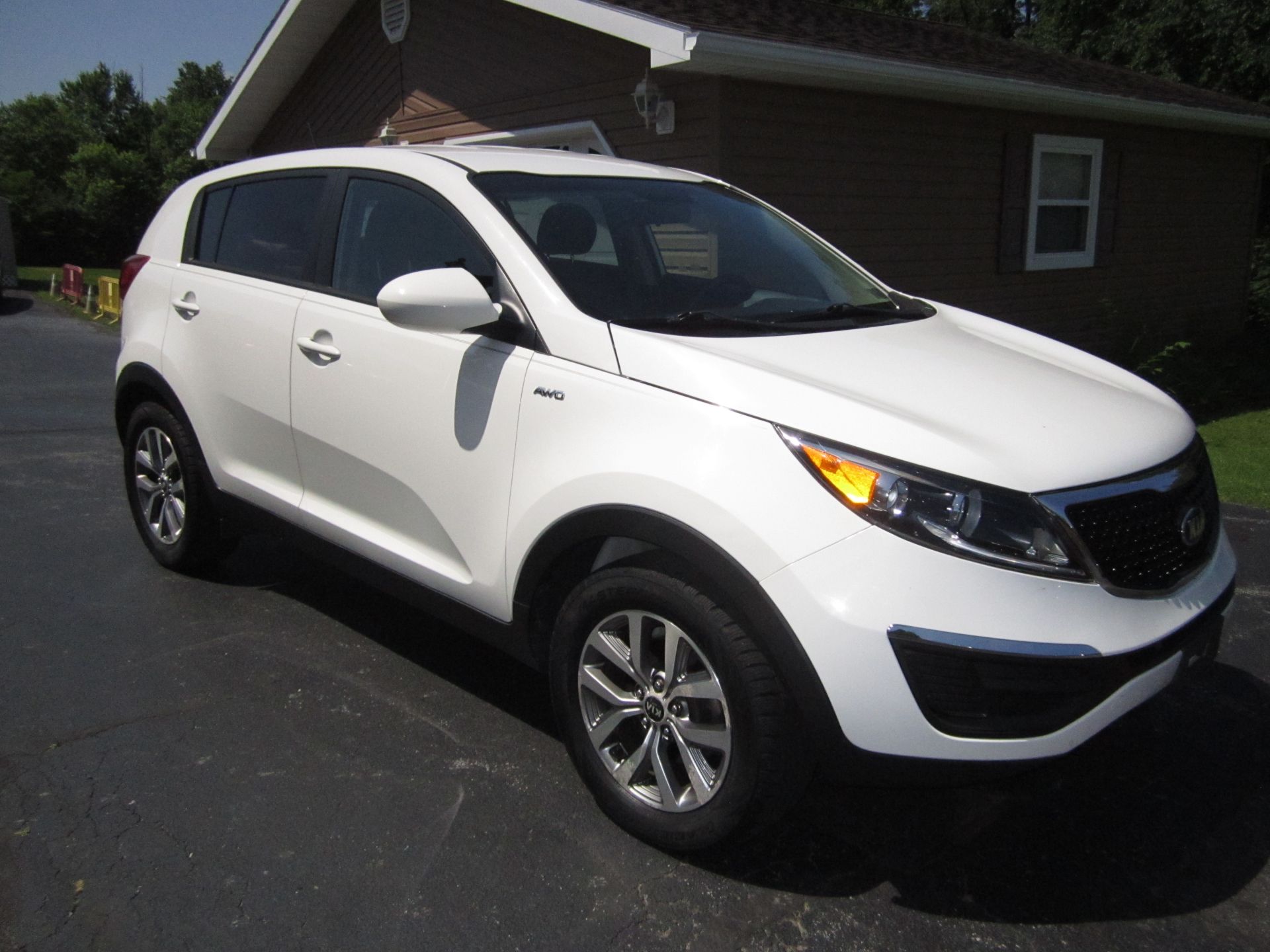 A white Kia Sportage SUV parked on an asphalt driveway in front of a brick house.