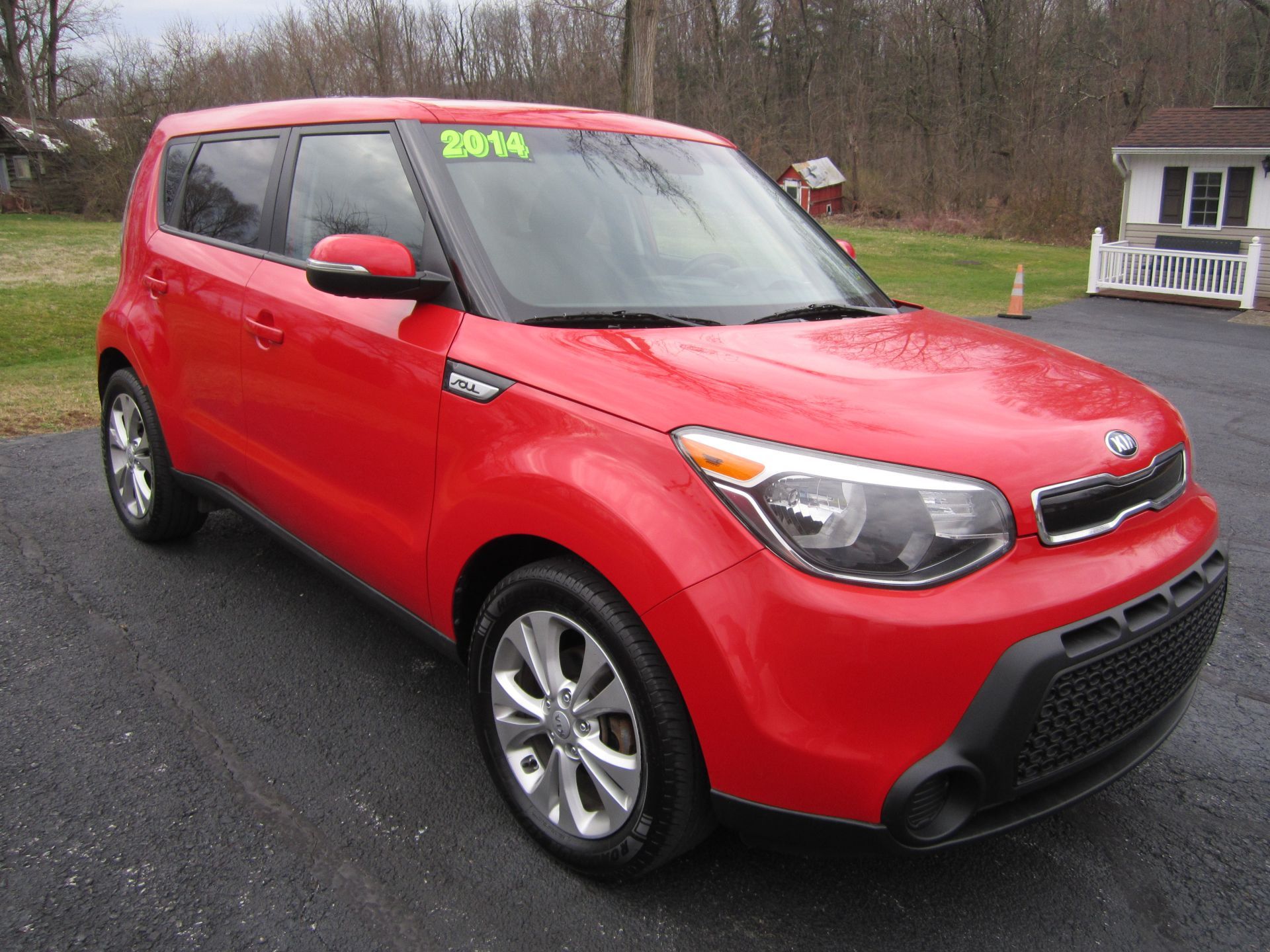 A red 2014 Kia Soul parked on an asphalt lot with a building in the background.
