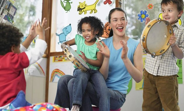 Children play musical instruments in a colorful classroom, smiling and clapping together.