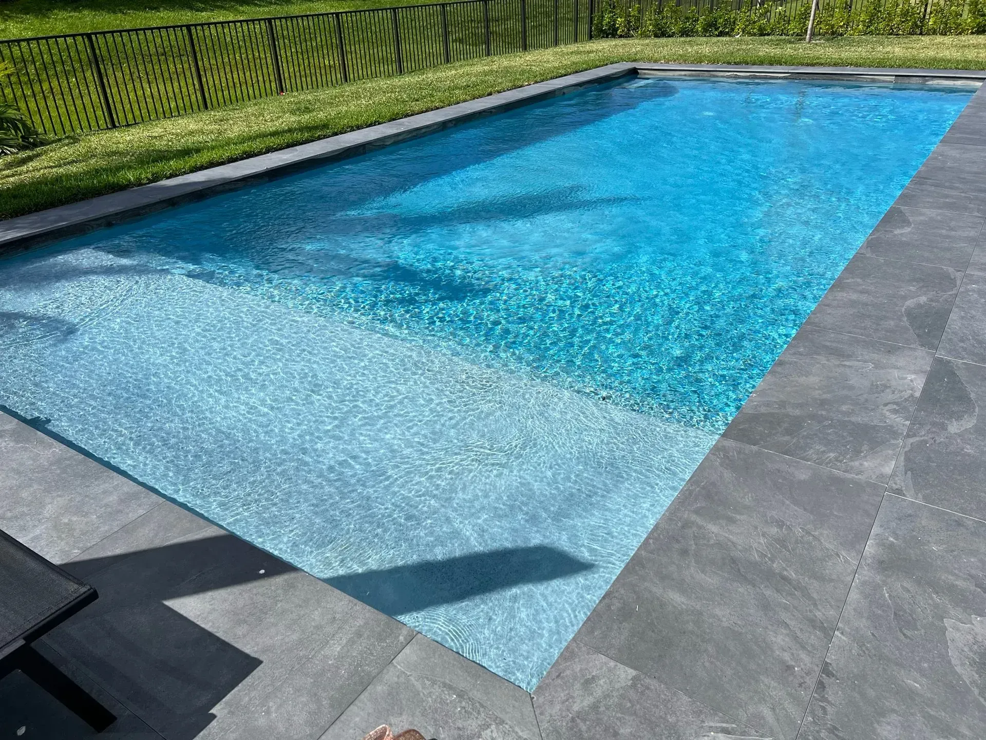 Rectangular swimming pool with clear blue water and stone patio.