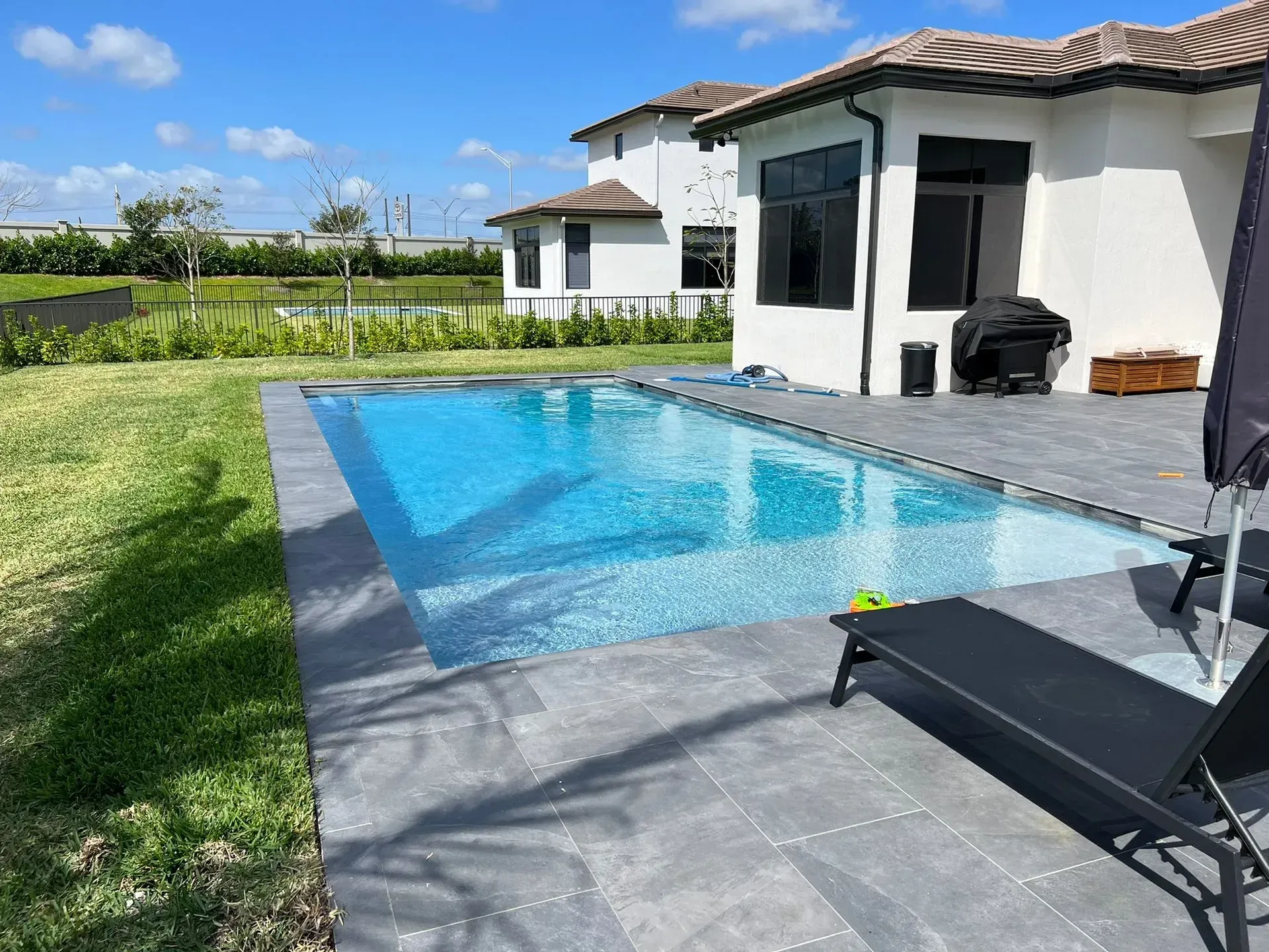 Rectangular pool with turquoise water, beside a white house, gray patio, and lawn.