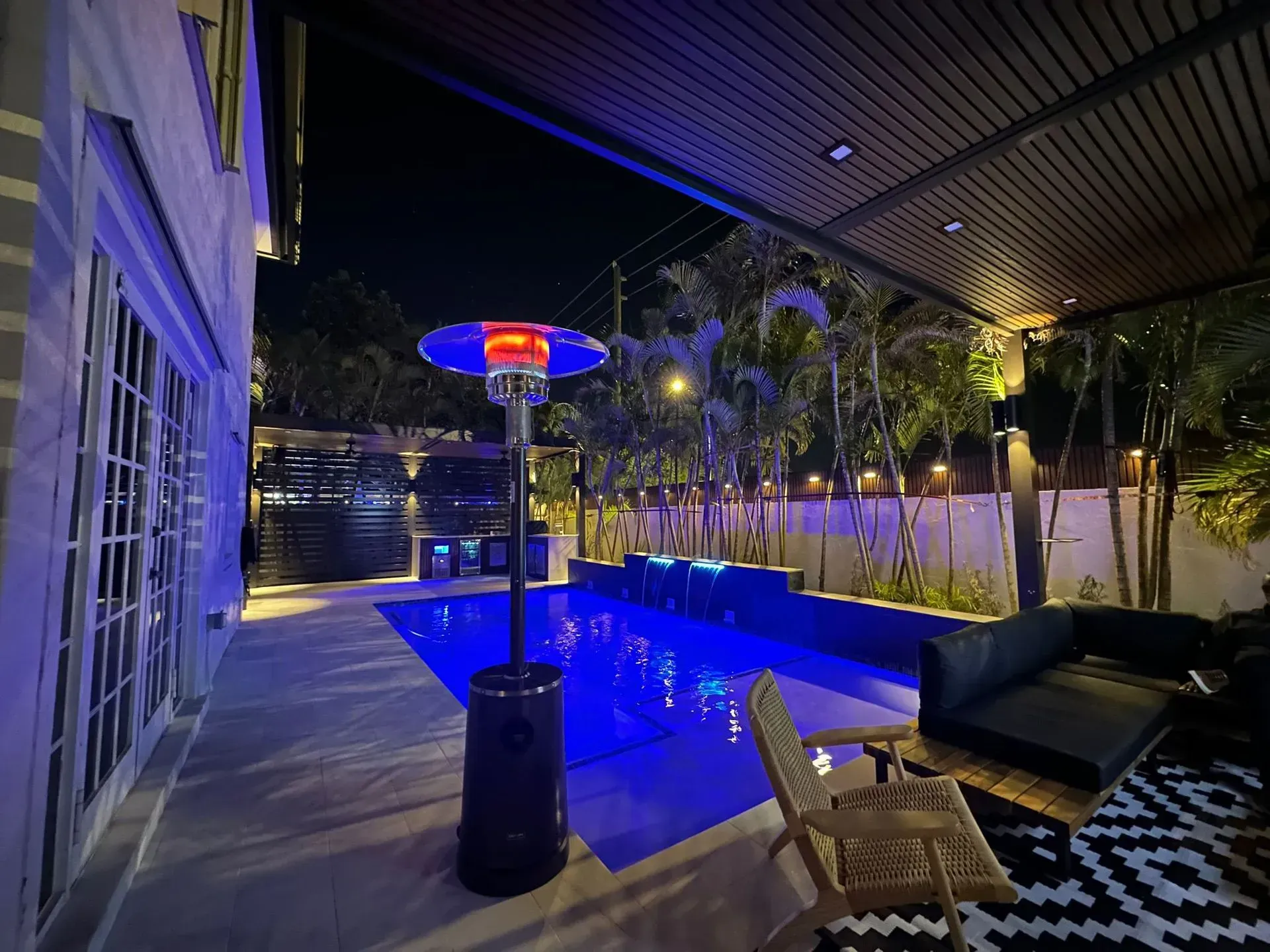 Night scene: outdoor pool, patio with heater, lounge seating, ambient lighting.