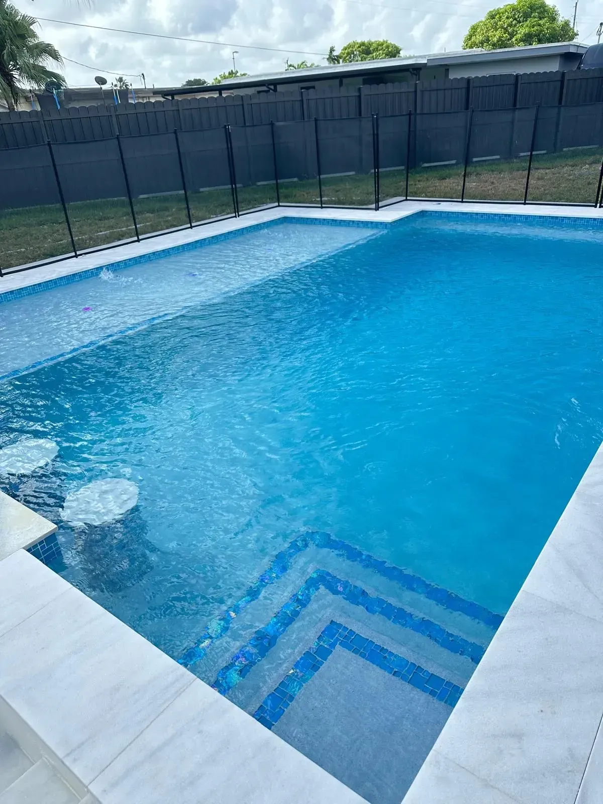 Blue swimming pool with steps, bar stools, and a black fence.