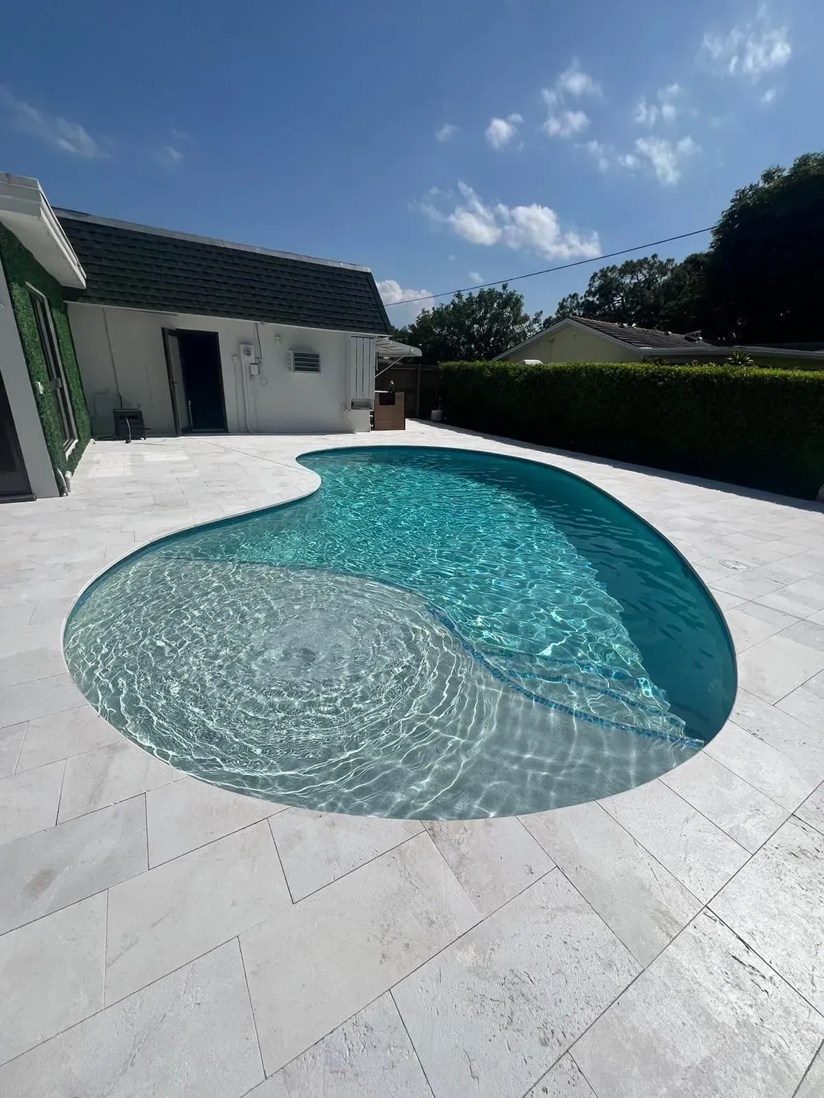 Pool with turquoise water in a white-tiled backyard on a sunny day.