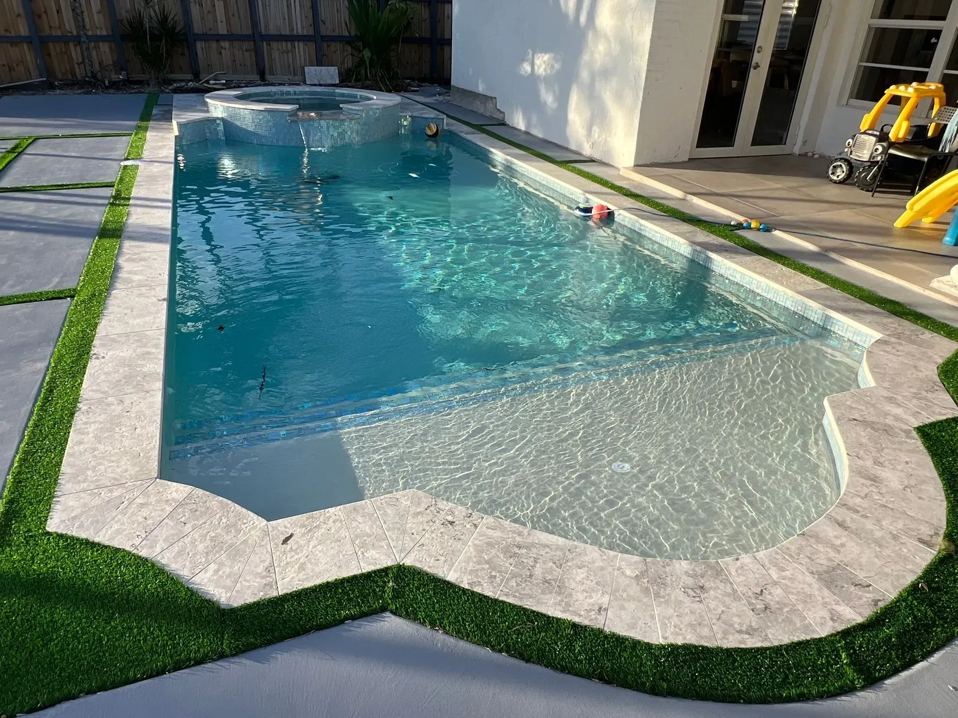 Rectangular swimming pool with light blue water, surrounded by stone and artificial grass.