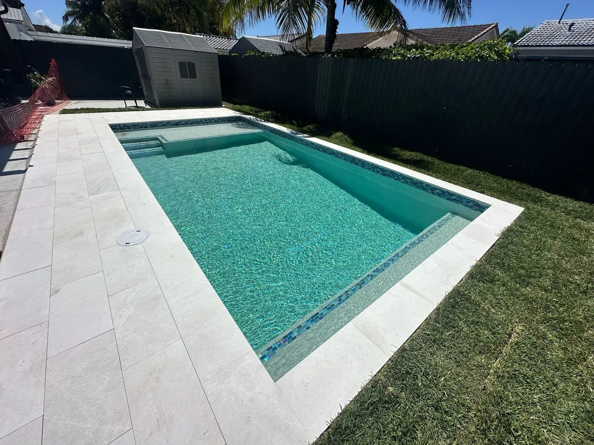 Rectangular swimming pool with light-colored tile surround and a tiled accent at waterline, surrounded by grass.