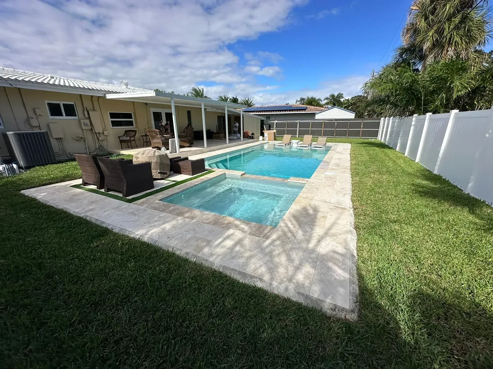 Backyard with a swimming pool and hot tub, green grass, white fence, and patio furniture.