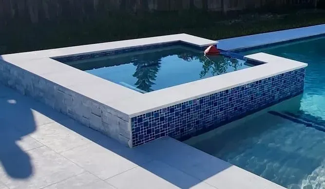 Pool with a raised spa, blue tiles, and white coping, reflecting the sky.