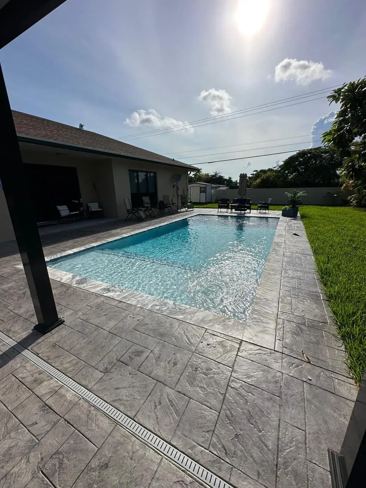 Swimming pool in backyard of a house on a sunny day. Concrete patio surrounds the pool.