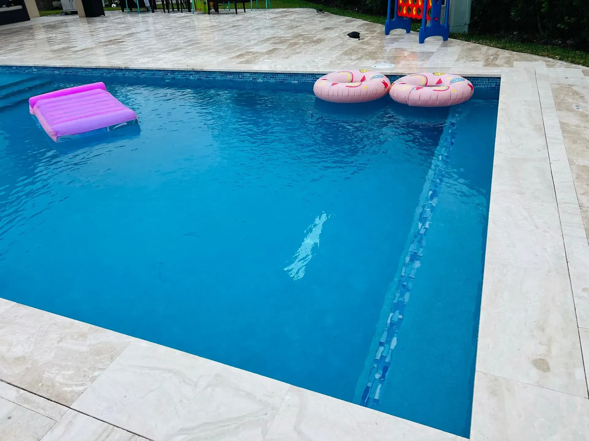 Swimming pool with floating raft and two pink inner tubes.