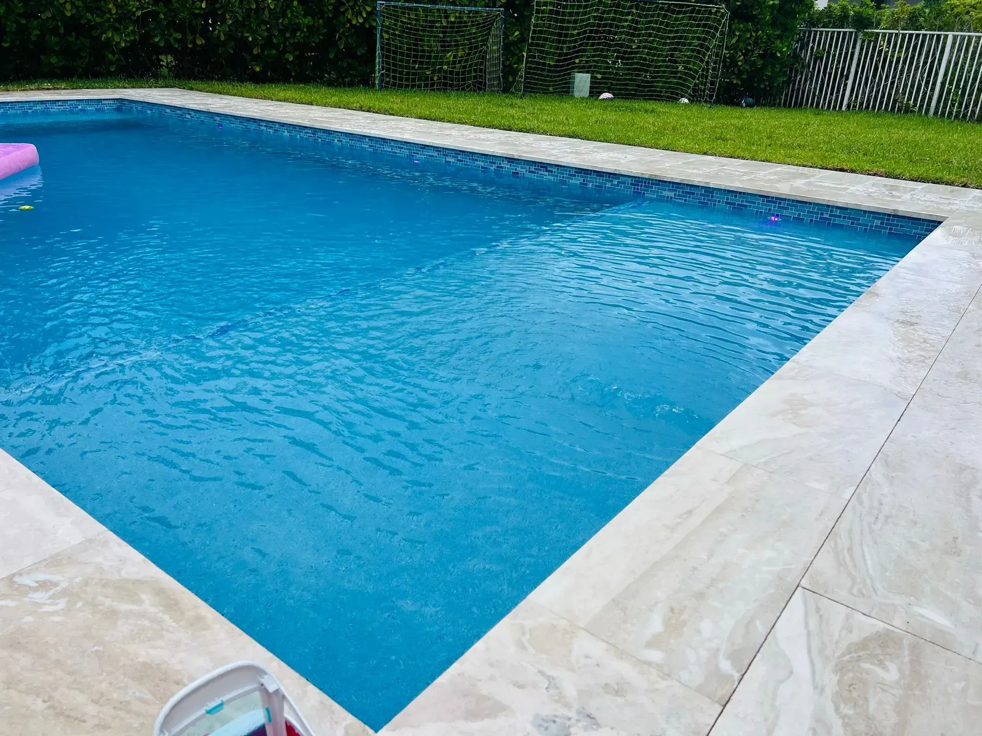 Swimming pool with blue water and beige tile surround, next to green grass.