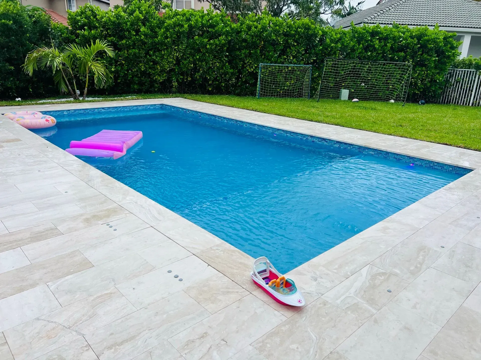 Pool with pink floatie, toy boat, and green lawn.