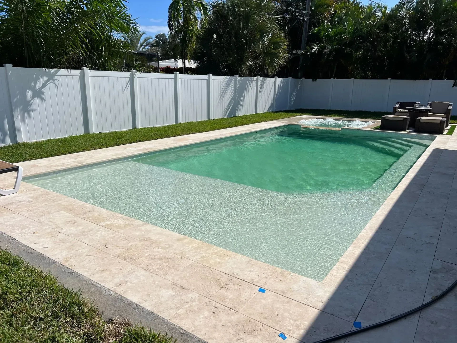 Rectangular swimming pool with clear water, surrounded by concrete and a white fence, in a backyard.