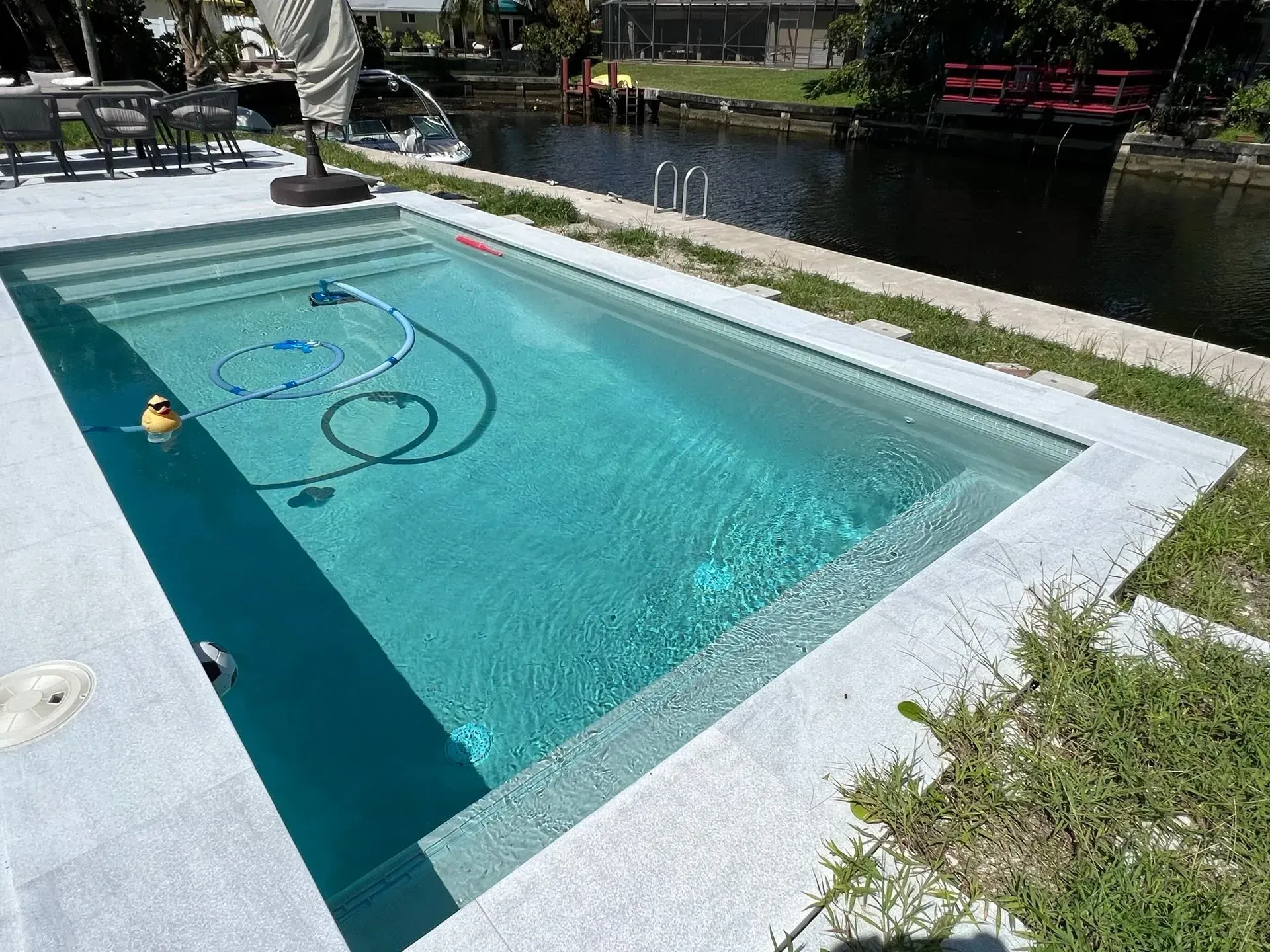 Rectangular outdoor pool with steps, next to a canal. White concrete surround and light blue water.